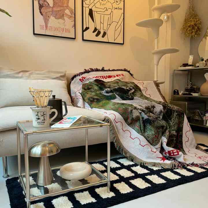 Natural modern living room featuring cream sofa, transparent glass side table, patterned rug, and cat tower creating a cozy atmosphere