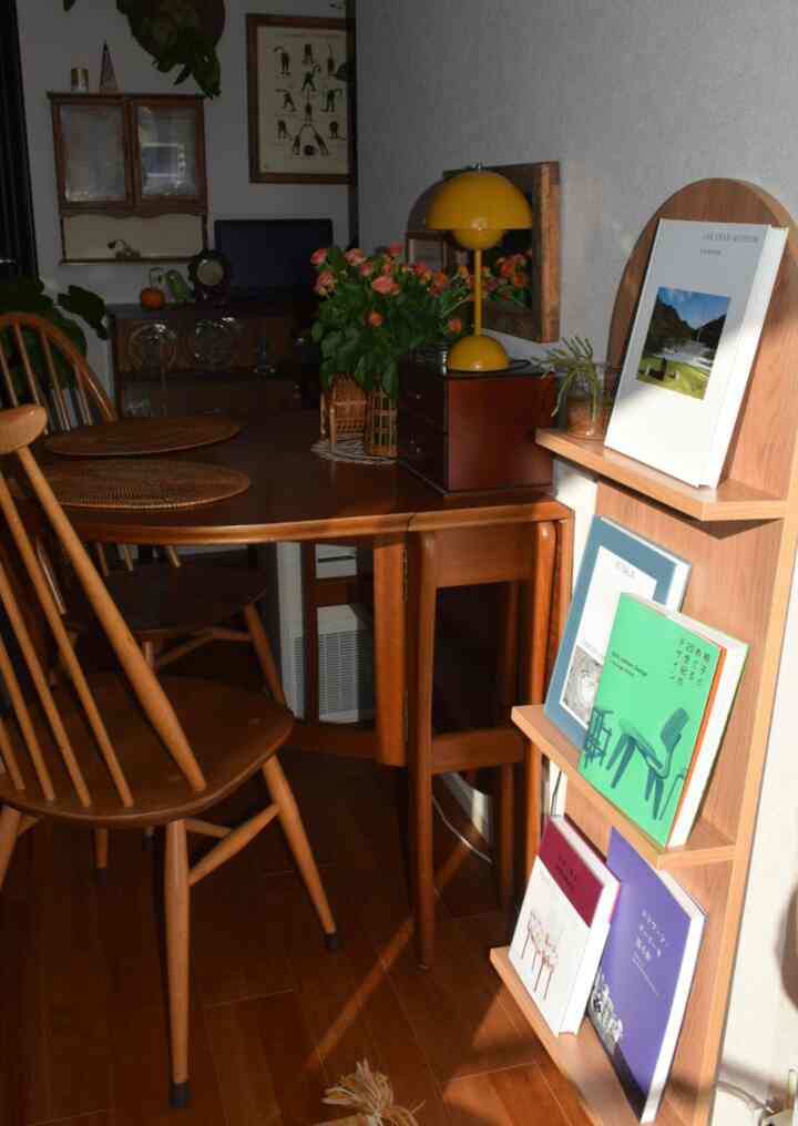 Wood tone light brown small dining space featuring vintage wooden dining table, chairs, yellow table lamp, and magazine rack with warm atmosphere