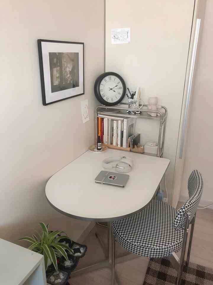 明るいホワイトトーンのホームオフィス空間、きれいに整えられたデスクと千鳥格子柄のチェア、ステンレス製のトロリー、額縁が配置された整理されたインテリア