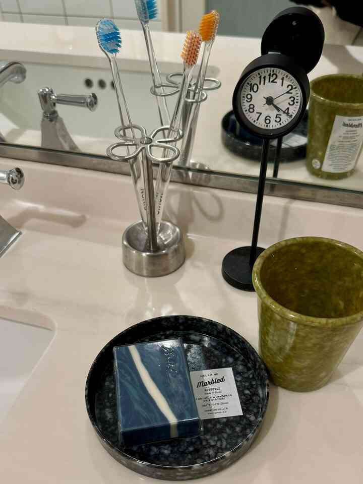 White and black toned bathroom sink area featuring toothbrushes, clock, and marbled tray arranged neatly