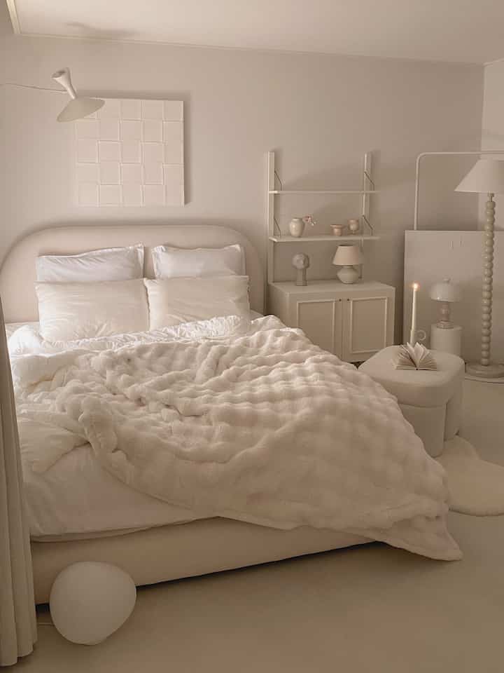 白とベージュのトーンの寝室、柔らかなベッド、ナイトテーブル、フロアランプが配置された落ち着いた印象的な空間