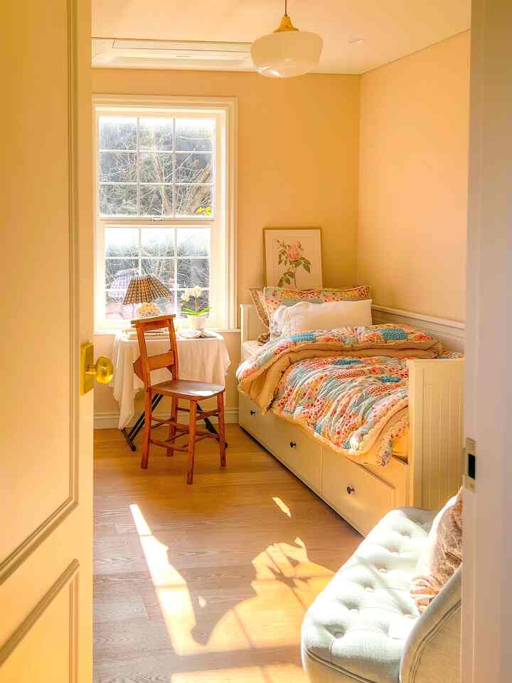 温かみのあるアイボリーとホワイトの寝室、ヴィンテージのデイベッドと木製の椅子が配置された日当たりの良い印象的な空間