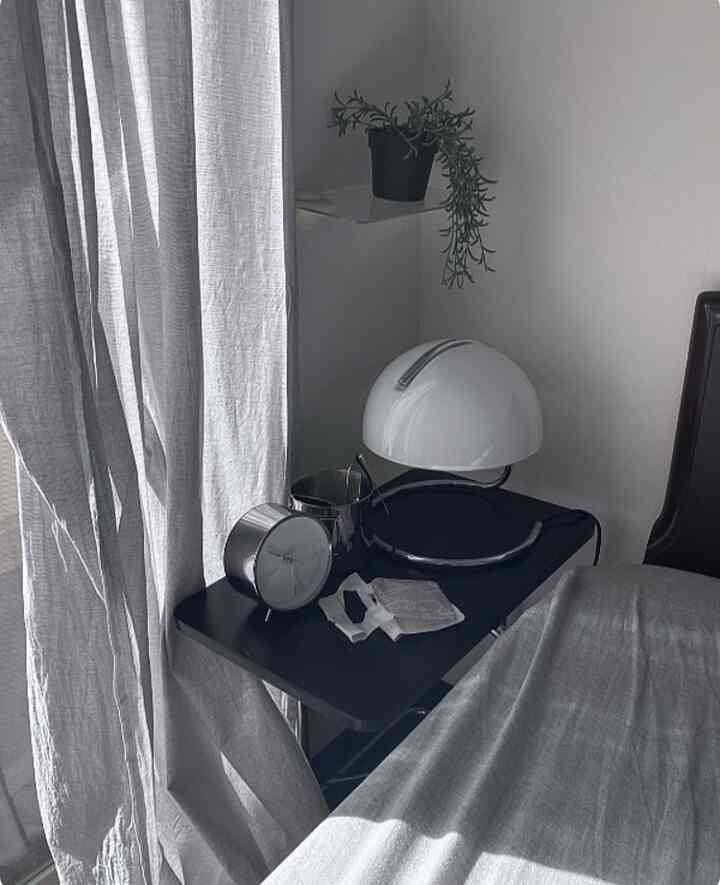 Gray and black toned bedroom featuring an IKEA side table with a silver alarm clock and white table lamp in a simple setting