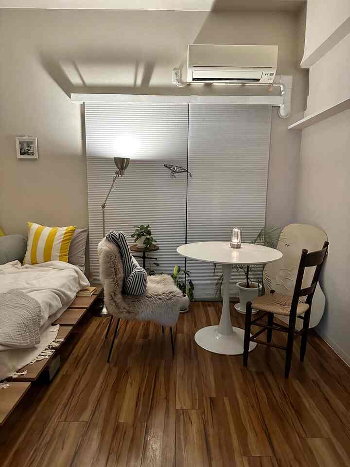 ナチュラルなブラウンの木目調フローリングとホワイトを基調としたワンルームのリビング、丸テーブルと椅子2脚、ソファとフロアランプが配置された落ち着いた空間