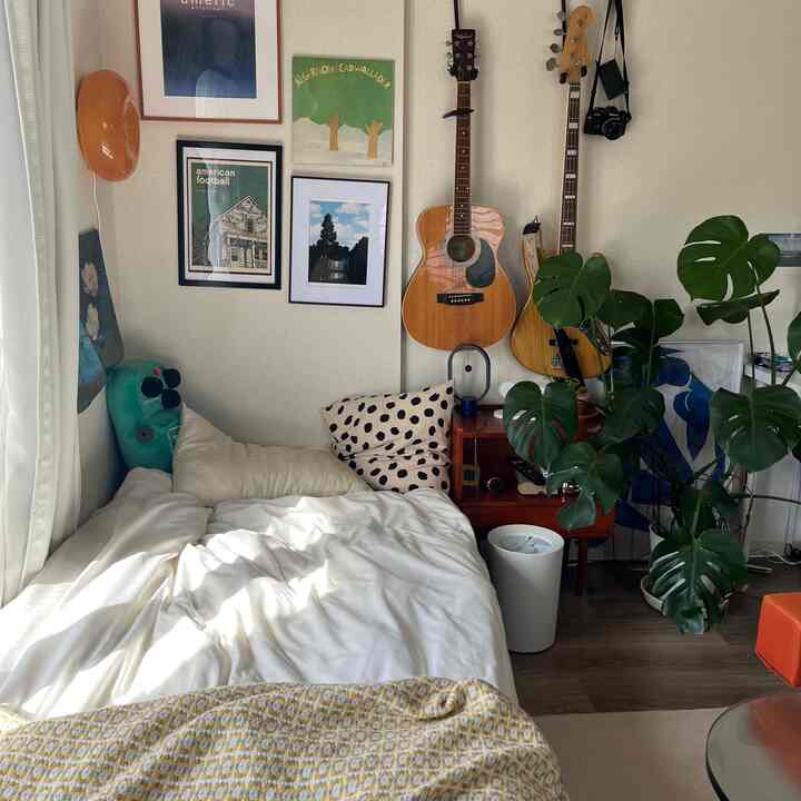 白とベージュのトーンの8畳の寝室、モダンな木製家具とモンステラの植物、ギターが配置された落ち着いた雰囲気のインテリア