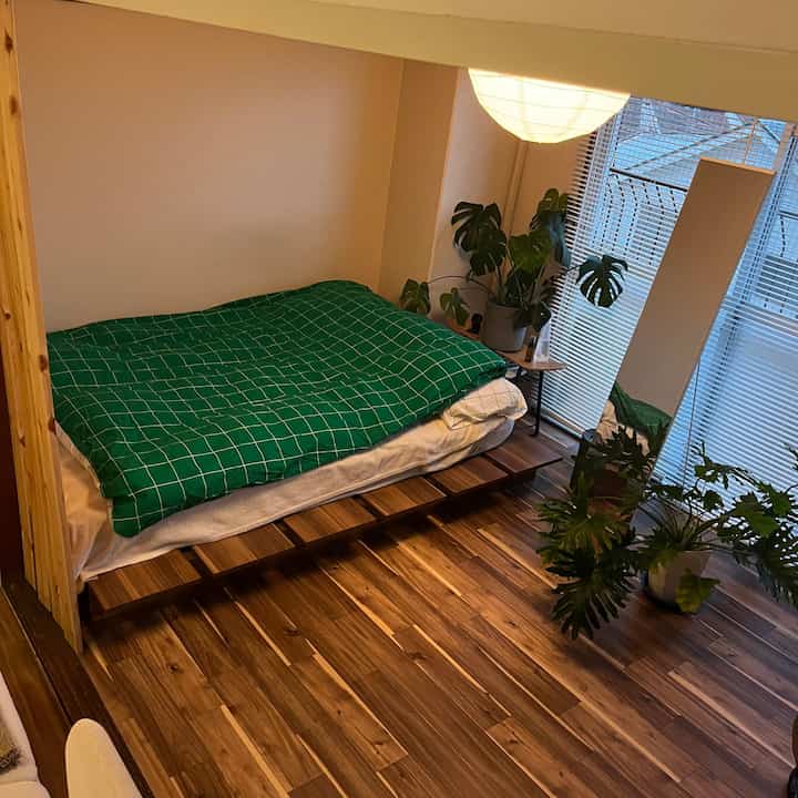 Natural-toned bedroom with wood-tone flooring and low bed frame, featuring lush foliage plants adding vibrancy