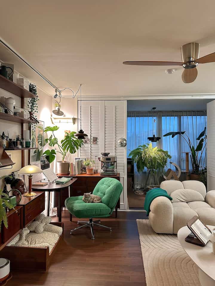 落ち着いたグリーンとナチュラルな木目調のリビング、ふかふかの回転アームチェアやソファ、植物が配置された雰囲気のあるインテリア