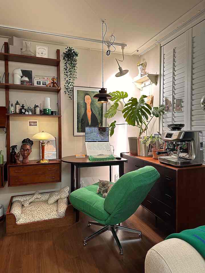 ウッドトーンとグリーンのダイニングルーム、ペンダントライトの下にある机に猫と植物が配置された雰囲気のある在宅勤務スペース