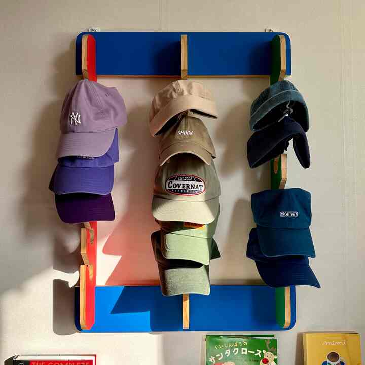 青色と木目調の壁掛け帽子ラックに様々な色の帽子が掛けられた寝室用収納スペース