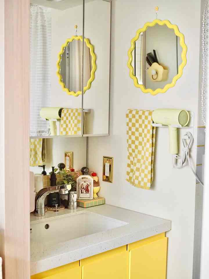 明るい黄色のトーンでまとめられた化粧台スペース、波型の鏡と黄色のドライヤーが印象的な清潔感のあるバスルームインテリア