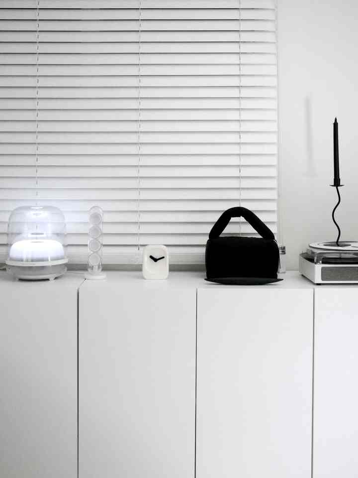 ホワイトとブラックのミニマルなインテリア、ホワイトのチェスト上にブラインドと装飾品が配置された空間