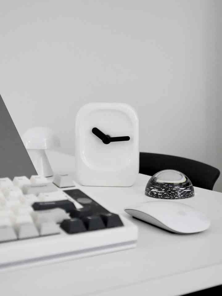 White-toned study space featuring a ceramic clock, Apple Magic Mouse, and keyboard on a minimal desk