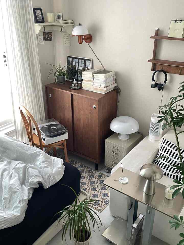 白い壁とソファ、木製家具と植物が配置された温かみのあるヴィンテージな寝室