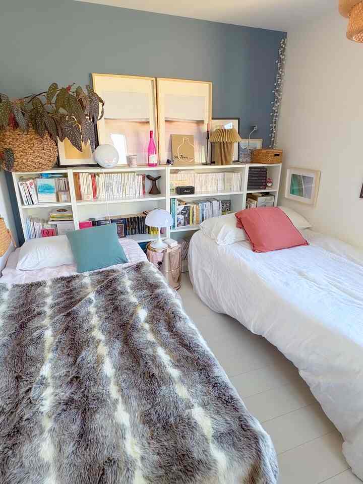 白と青の色調の寝室、二つのベッドと本棚が配置された雰囲気のあるインテリア