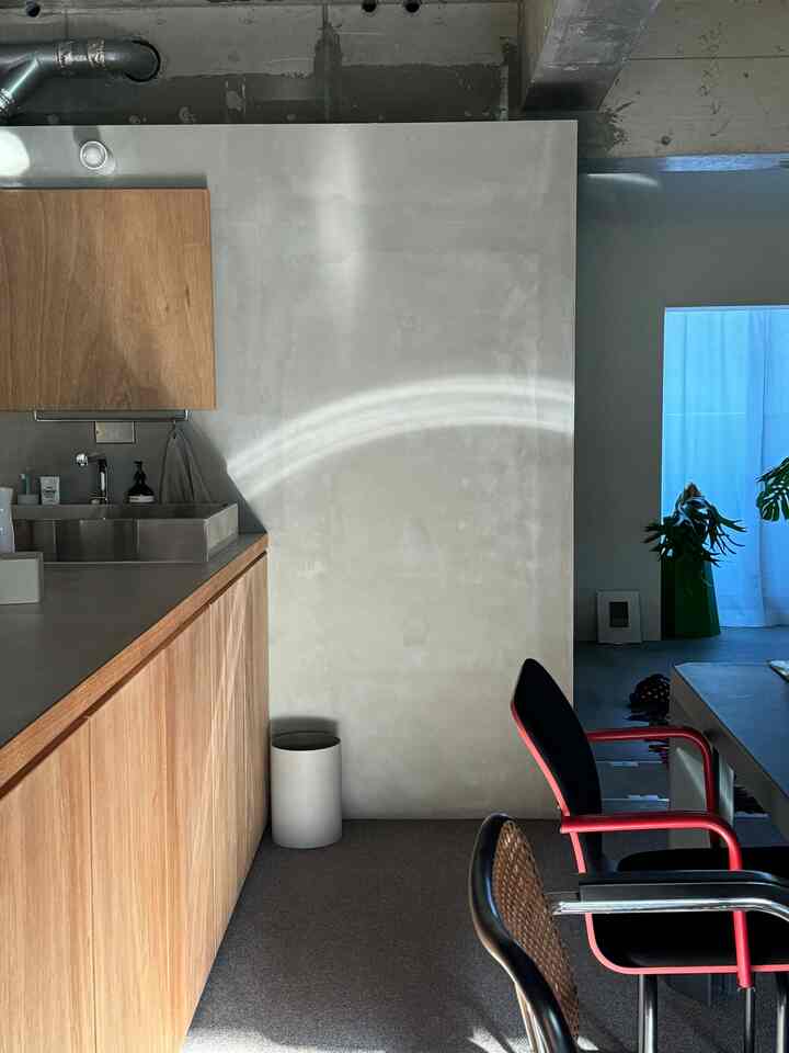 ナチュラルカラーのモダンなキッチン空間、グレーのカーペットと木製キッチンキャビネット、赤いアームチェアが配置された印象的なインテリア