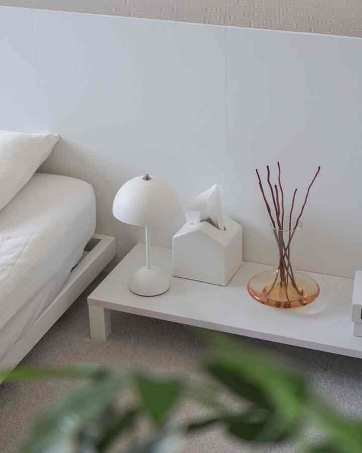 白を基調とした寝室、ナイトテーブルの上にテーブルランプとディフューザーが置かれた、清潔感のあるインテリア