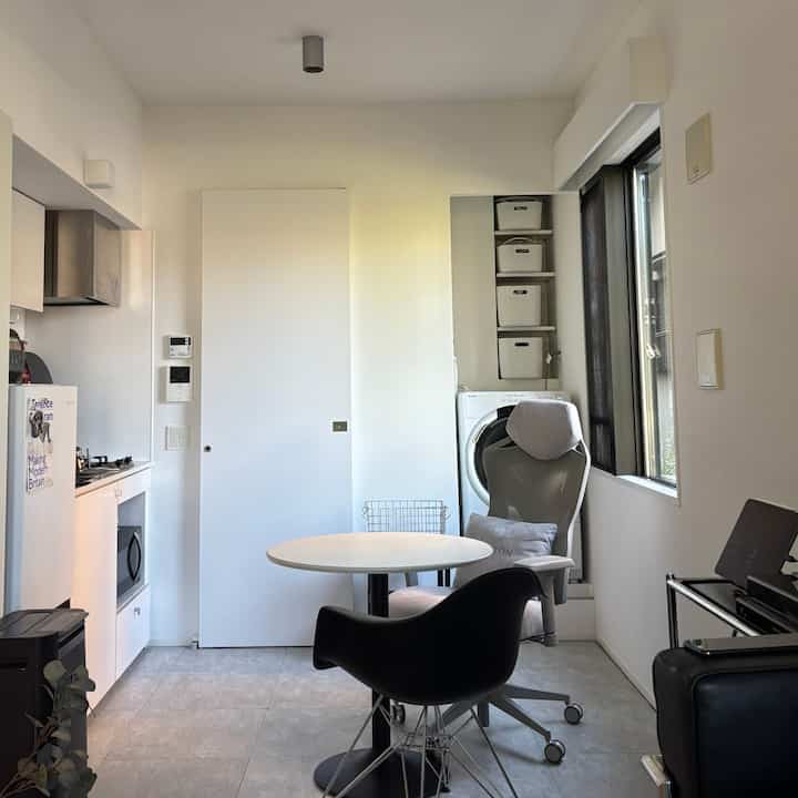 ホワイトトーンのキッチンとリビングが融合した一人暮らし向けコンパクトな部屋、丸いダイニングテーブルとオフィスチェアが配置されたモダンで清潔感のある空間