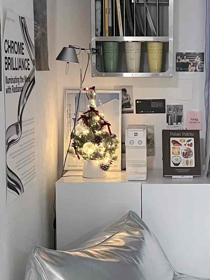 白とシルバーのトーンでまとめられた狭い部屋のコーナーにミニクリスマスツリーや壁掛け照明、壁デコが配置されたミニマルな雰囲気のインテリア