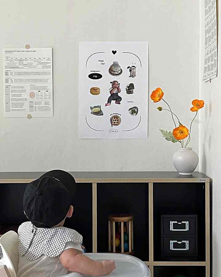 A natural and clean kids' room with white walls, black bookshelf, cute poster on the wall, and vibrant orange flowers