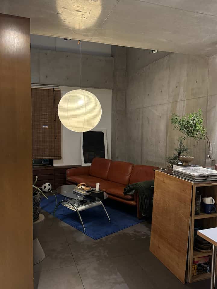 温かみのある木目調とブルーのラグが調和するヴィンテージなミッドセンチュリーモダン風リビング、茶色のレザーソファと中央の照明が配置された空間