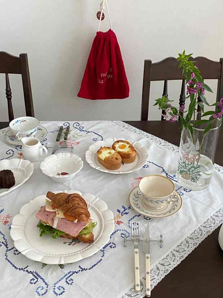 白いテーブルクロスのダイニングテーブルにホームカフェのセットとカトラリーが配置された雰囲気のあるインテリア