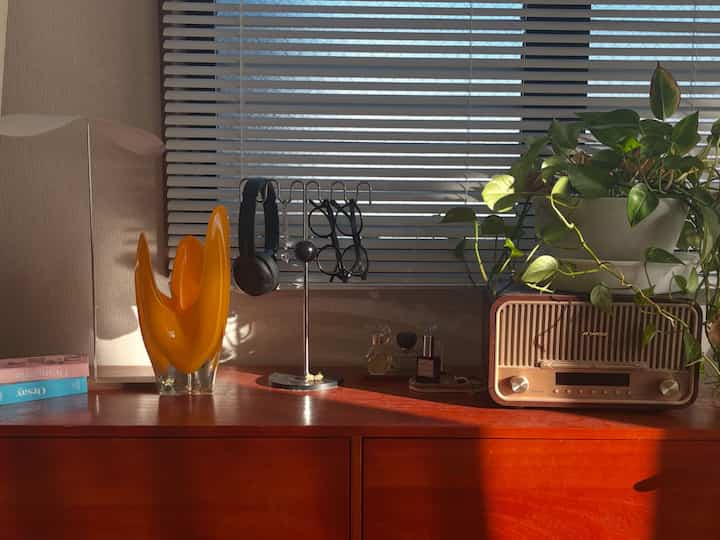 温かみのあるレッドウッド調の8畳の一人暮らし空間、窓際に植物とヴィンテージラジオ、装飾品が配置された落ち着いたインテリア