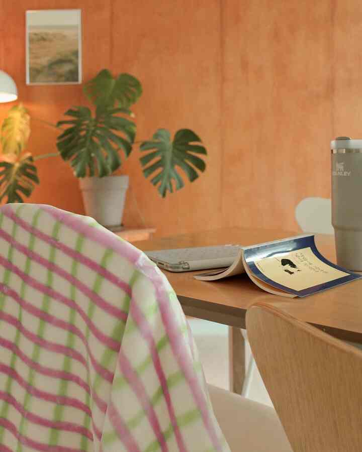 ナチュラルな木目調の壁と植物が調和したダイニングルーム、チェック柄の毛布とタンブラーが置かれたデスクが落ち着いた雰囲気を演出している