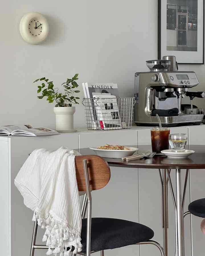 White and gray toned kitchen featuring wooden dining table with chairs and a Breville espresso machine in a simple home cafe setting