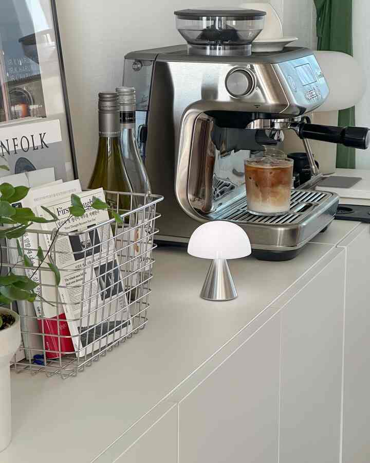 White and silver toned kitchen space featuring an espresso machine and LED mushroom lamp on a clean countertop, evoking a neat home cafe atmosphere