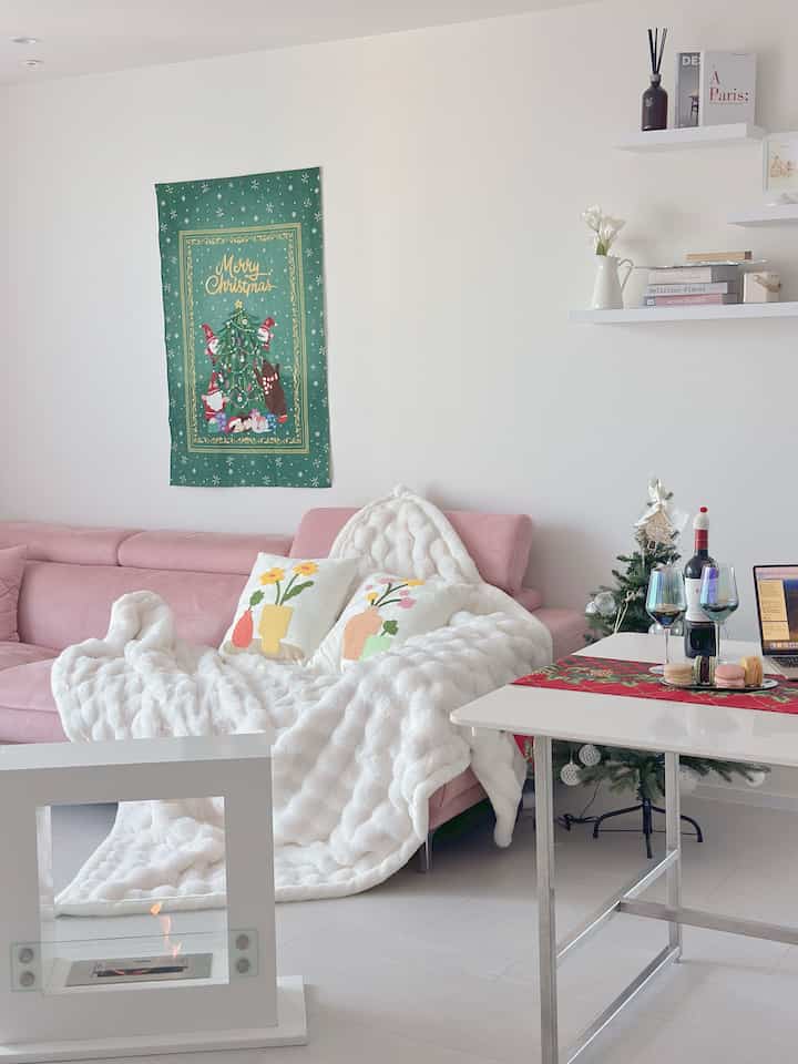 White and pink toned living room featuring a pink sofa, Christmas decorations, and a cozy white blanket creating a warm atmosphere