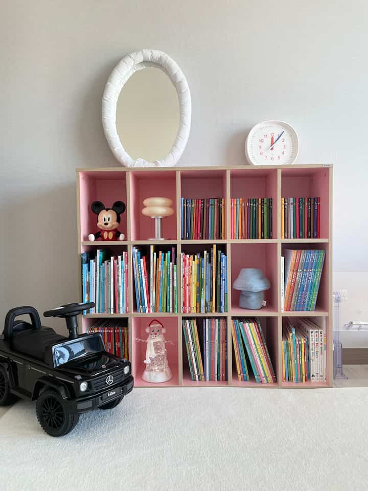 Kids' room dominated by pink bookshelf with a white rug and a toy car placed in front, creating a cozy atmosphere
