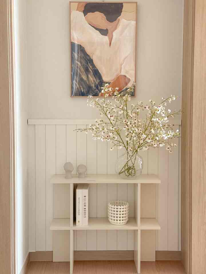 Natural beige and wood tone entrance featuring a small bookshelf with a vase of flowers and framed art, creating a clean and serene atmosphere