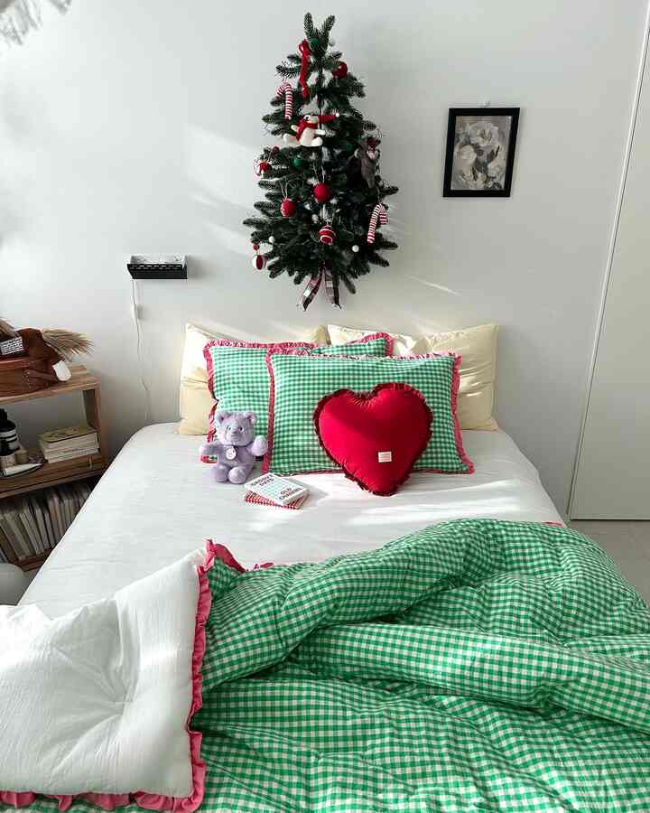 A modern cozy bedroom space with white walls and floor, featuring green checkered bedding and cushions.
