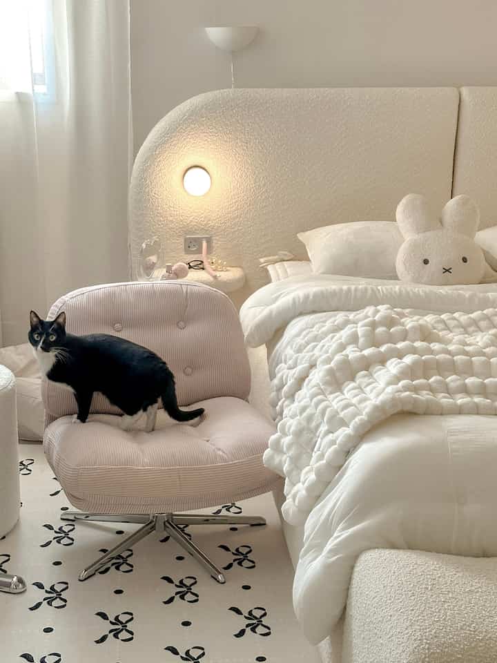 Beige and white toned bedroom featuring a soft pink armchair with a cat, creating a simple and natural atmosphere