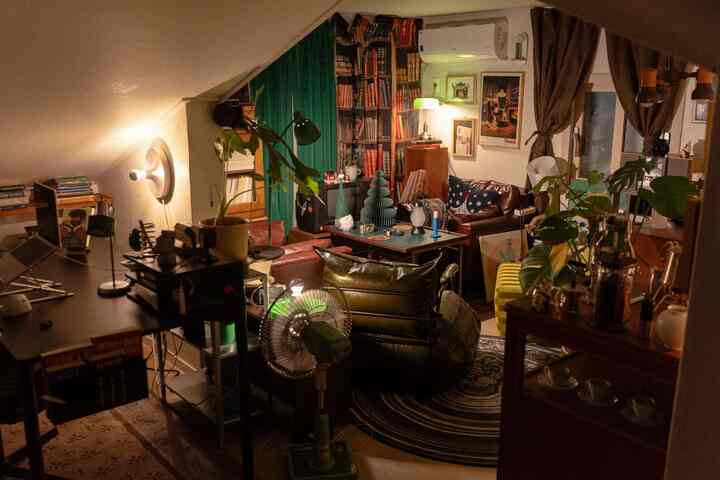 暖かいブラウンとグリーンのトーンが調和するロフトのワンルームリビング、ヴィンテージ家具と植物、デスクが配置された雰囲気のある空間