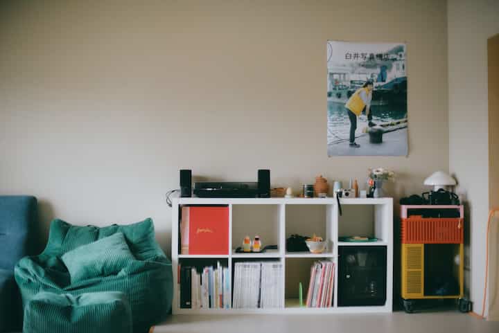 Natural beige-toned living room featuring a white shelf and green bean bag, with retro poster creating a cozy atmosphere
