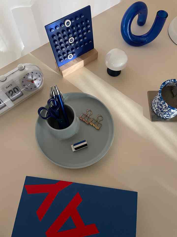 ブルーとスカイグレーの色調のデスクスペース、カレンダーやペン、トレイなどのミッドセンチュリーモダンな小物が配置された印象的なワークスペース