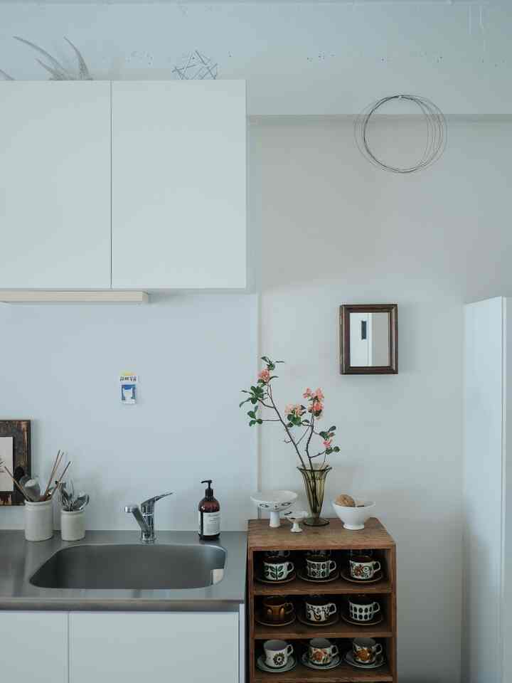 White and wood tone kitchen space featuring a vase with flowers and neatly arranged tableware, lending a clean and calm atmosphere