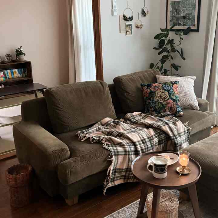 Natural brown toned living room featuring a large sofa with blanket, plant, side table, and candle creating a warm atmosphere