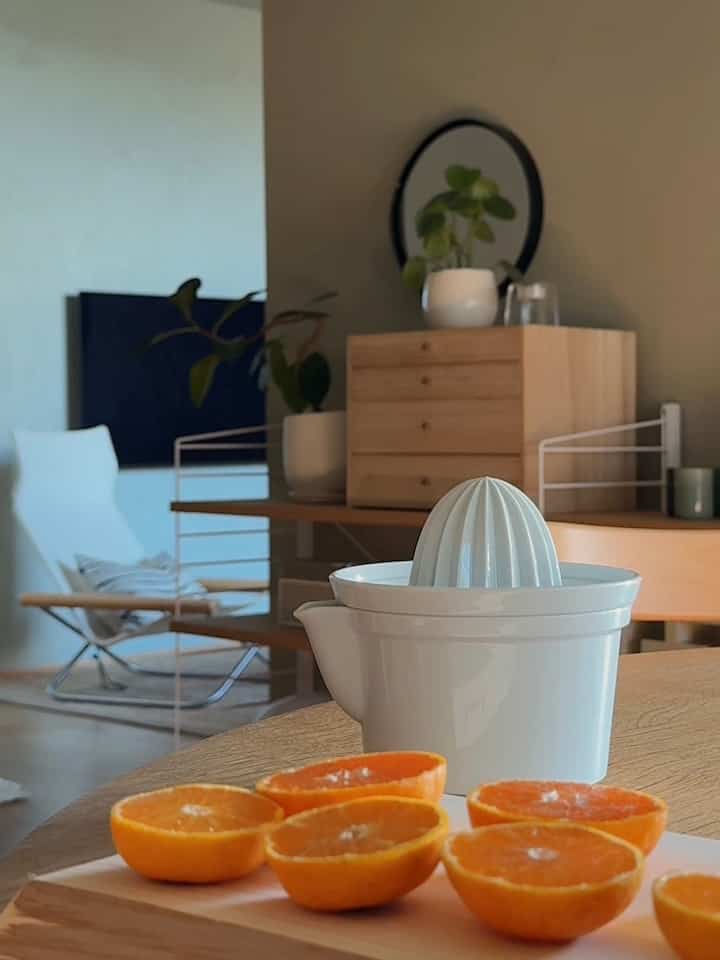 ナチュラルな木目調とオレンジ色が調和するダイニング、ミニマルな家具と朝のジュース準備がある雰囲気のインテリア