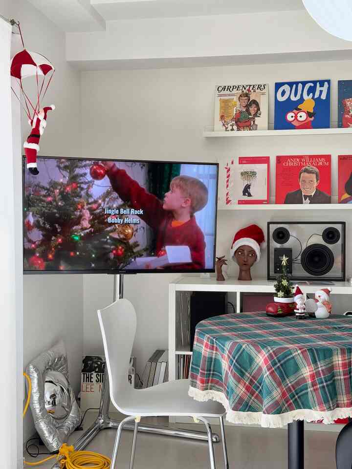 白い壁のリビングルーム、透明なスピーカーとクリスマスデコレーション、チェック柄のテーブルクロスが配置された雰囲気のあるインテリア