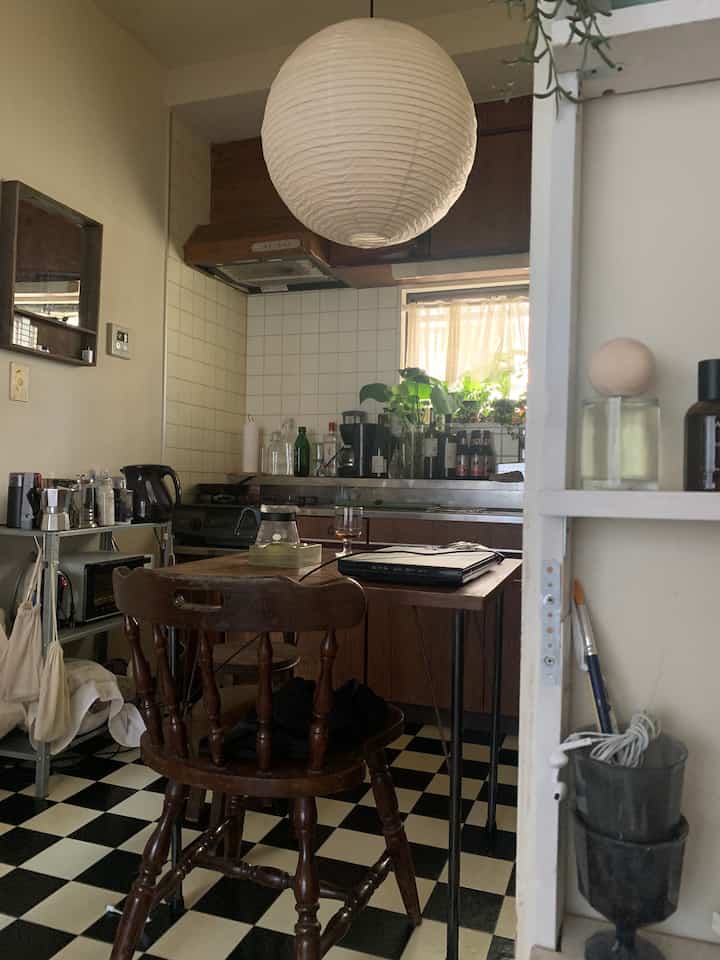 白と木目調が調和したワンルームのキッチン空間、チェック柄の床とペンダントライトが配置された雰囲気のあるインテリア