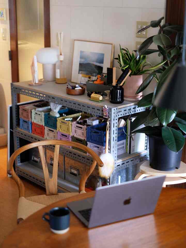 A wood tone and gray themed dining room combined with a home office featuring a laptop and organized storage crates, creating a tidy space
