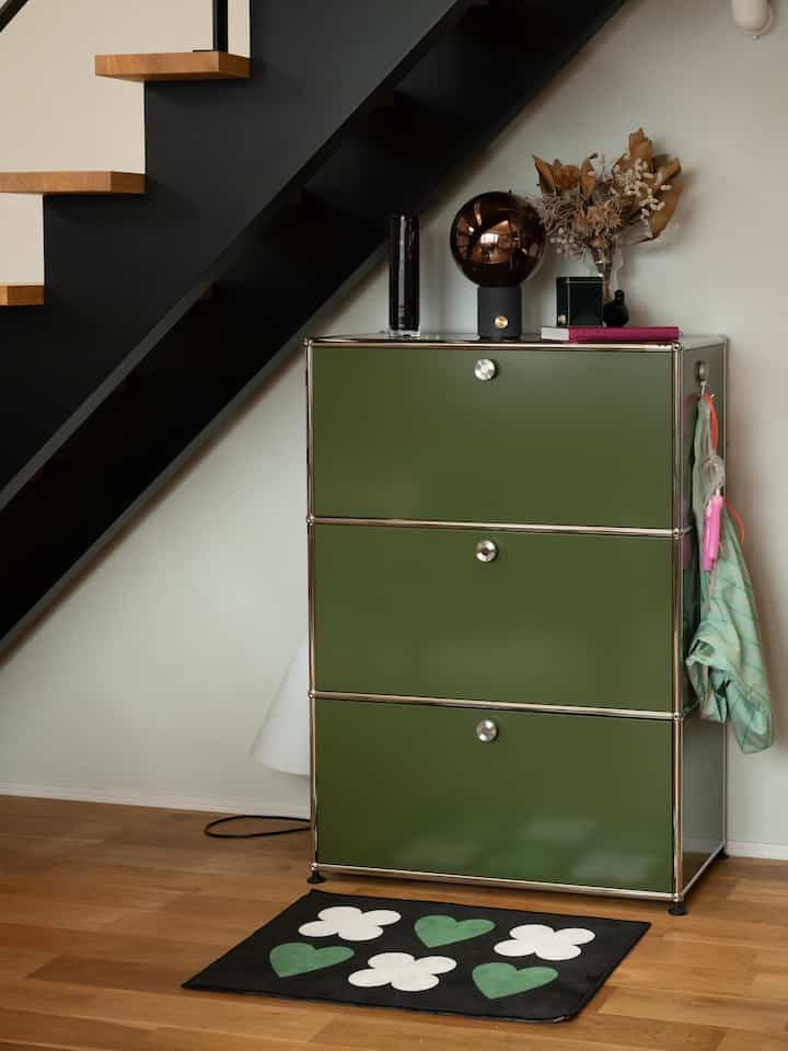 モダンな玄関、黒い階段下に緑のキャビネットと白と緑の模様がある黒いラグが配置された雰囲気のあるインテリア