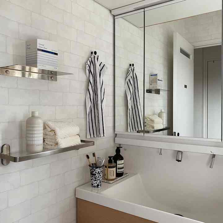 White and wood tone bathroom featuring a sink, mirror cabinet, and shelves with neatly arranged towels and toiletries
