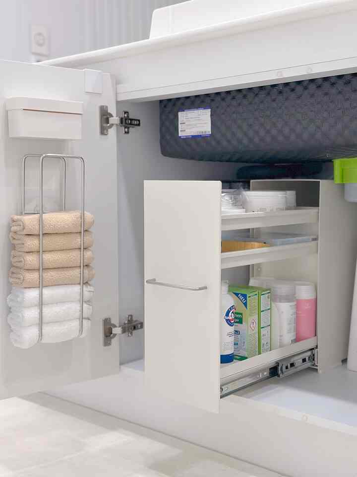 白とベージュの色調のキッチンシンク下収納、きちんと整理されたタオルと衛生用品が配置されたコンパクトな空間