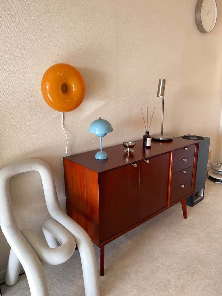 Beige tone walls and floor with wood-tone shelf and unique curved chair in a Mid-Century Modern style living room