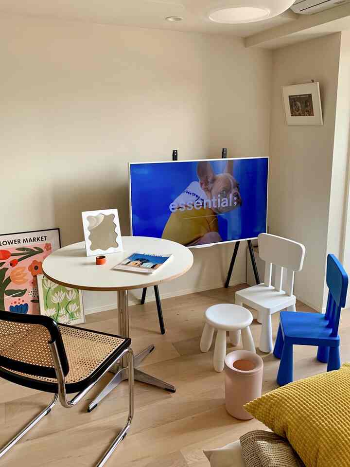 A simple modern living room with white and wood tones, featuring a round dining table, kids' chairs, and a TV on a stand
