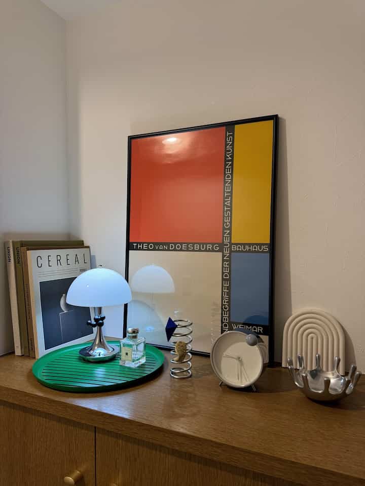 ミッドセンチュリーモダンスタイルの玄関、木目調のコンソールに白いテーブルランプとカラフルなポスターフレームが配置されたすっきりとした空間