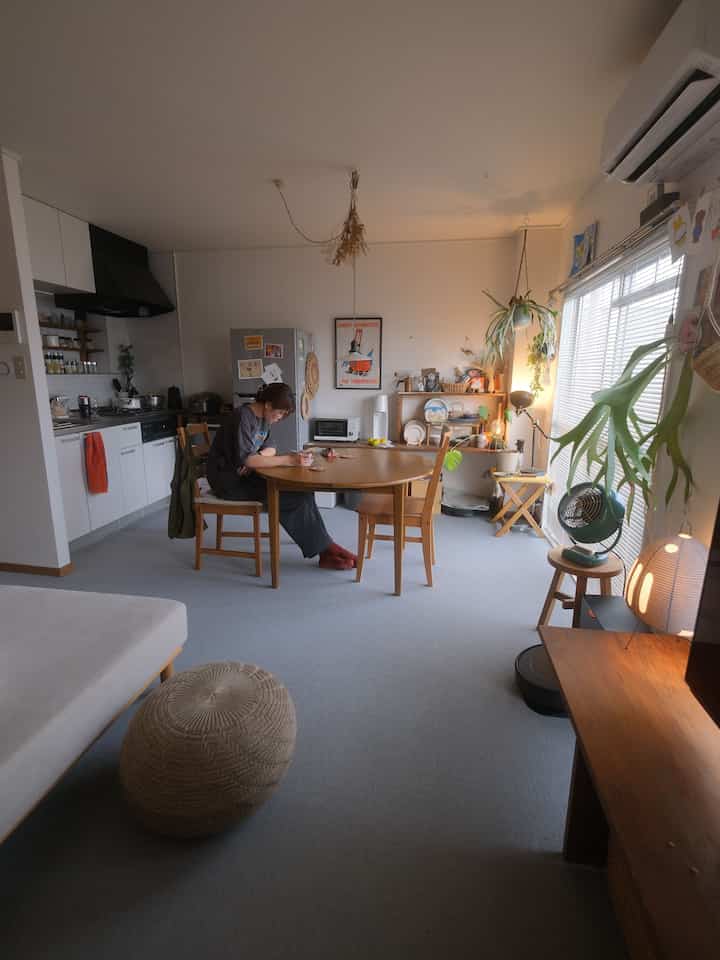 ライトグレーのカーペット床に木製の円形テーブルと椅子が配されたナチュラルな雰囲気のキッチン兼ダイニングルーム